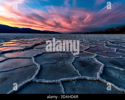 Badwater Basin salt flats in Death Valley National Park, California, at sunset after a rare rain, reflecting the sky in natural salt polygons. Stock Photo