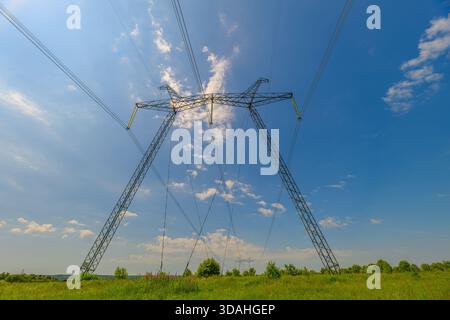 A breathtaking and striking view of power lines extending across a lush green field, all underneath a vibrant blue sky Stock Photo