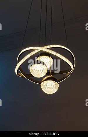 A contemporary chandelier featuring three glowing glass spheres encased in sculptural, looping illuminated metal bands, suspended elegantly from the c Stock Photo