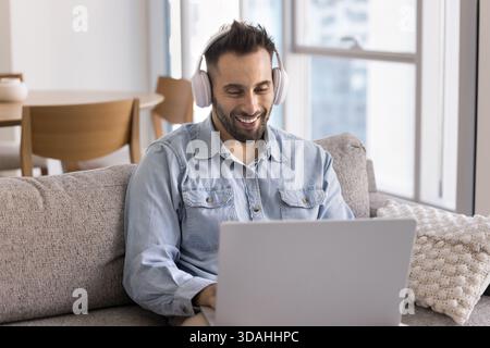 Smiling man wearing headphones working on laptop from home Stock Photo