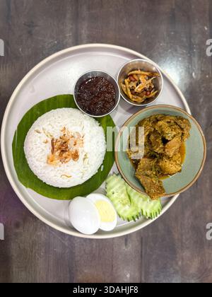 A beautifully plated Nasi Lemak featuring fragrant rice on banana leaf, beef rendang, sambal, egg, cucumber, anchovies, and peanuts—an iconic Malaysia Stock Photo