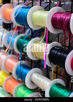 Vibrant assortment of colorful thread spools and cord for craft project. shiny sewing supply collection sits on display rack with blurred background Stock Photo