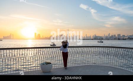 silhouette of a woman on bridge with Dubai skyline background at sunset, she is pointing at the iconic Burj Khalifa, 4k winter Dubai skyline views at Stock Photo