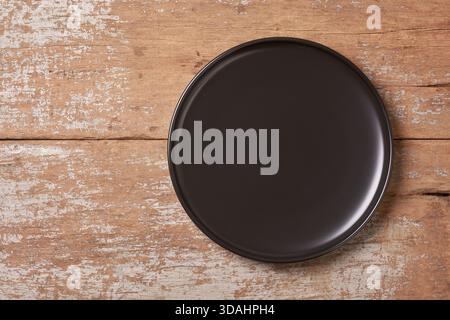empty matte black ceramic plate on weathered rustic textured wooden surface with peeling paint, mock-up template for graphic designing with copy space Stock Photo