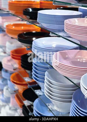 Low angle view of colorful plastic plates and bowls neatly stacked on glass shelf in store display. This kitchenware offers an abundance of choice and Stock Photo