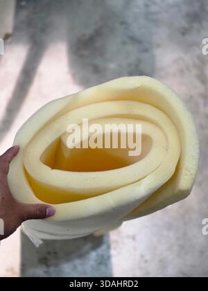 Close up of hand holding soft yellow foam roll for an upholstery project. Flexible material with thick texture, sheet for comfortable furniture or new Stock Photo