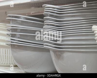 Neat stack of white plastic bowls and modern square plates on shelf in store. This simple kitchenware and dinnerware display shows an orderly and clea Stock Photo