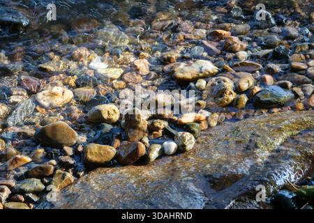 Small stone cairn balanced in clear flowing stream over wet pebbles. natural riverbed creates serene, tranquil background, evoking feeling of peace an Stock Photo