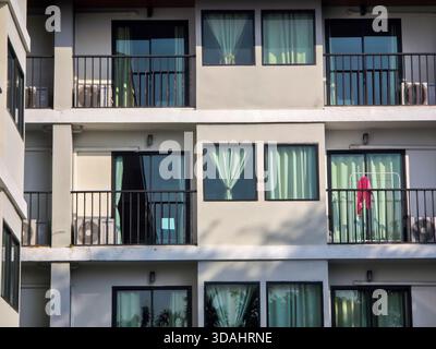 Modern apartment building exterior with minimalist architectural design. Facade features multiple floors, private balconies with black railings, and l Stock Photo