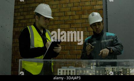 Two construction workers in vests and hard hats reviewing plans on site Stock Photo