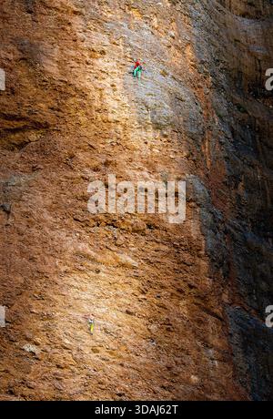 Conceptual shot showing the immense scale of a cliff compared to tiny human figures, representing resilience, determination, and overcoming obstacles Stock Photo