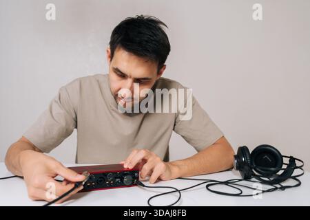 Portrait of audio engineer male holding red usb audio interface card and plugging cable into headphone output, setting up for music creation, sound Stock Photo