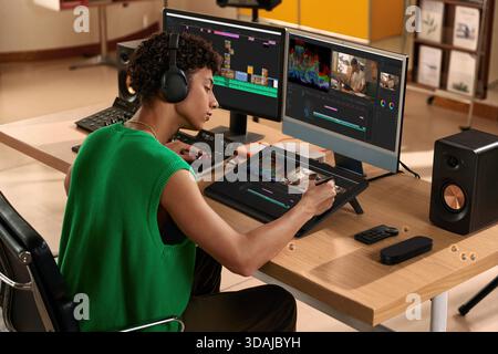 Young male video editor wearing headphones working on video project using graphics tablet and color grading panel Stock Photo