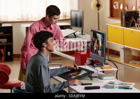 Two creative professionals collaborating and discussing image editing project on computer screen using graphics tablet Stock Photo