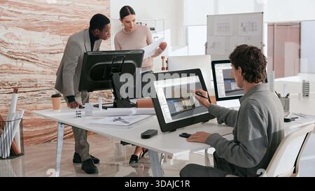 Team of architects discussing 3D building render on large graphics tablet in modern architectural firm Stock Photo