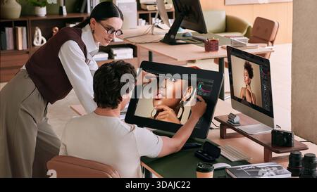 Creative director reviewing photo retouching work on graphics tablet with male editor in modern office Stock Photo
