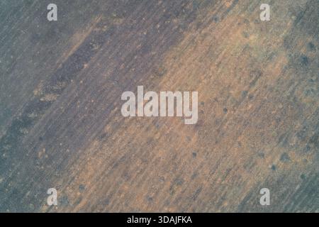 Aerial drone shot of a rough field surface featuring a mottled blend of dark grey and rust-orange soil colors. Diagonal agricultural texture and environmental background pattern in a rural landscape area. Stock Photo