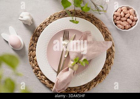 Soft Easter table setting with pink plate, linen napkin, gold cutlery and spring accents. Elegant pastel holiday composition. Stock Photo