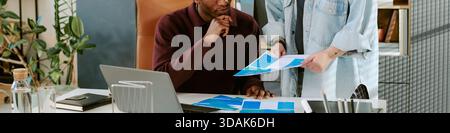 Young Black Man Sitting at Desk Reviewing Documents with Caucasian Woman Stock Photo