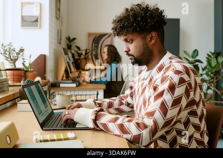Young Adult Black Man Focusing on Laptop While Working in Contemporary Office Stock Photo