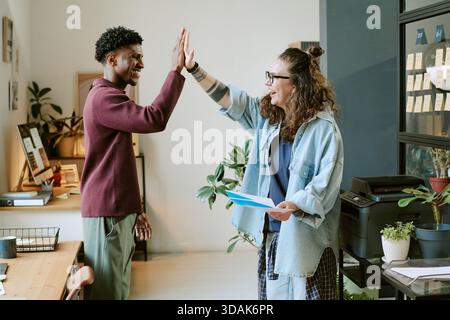 Young Caucasian Woman and Young Black Man Celebrating Success in Office Stock Photo