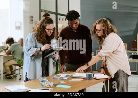 Young Caucasian Women and Black Man Collaborating on Creative Office Project Stock Photo