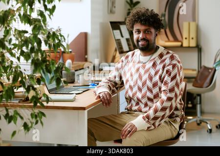 Portrait of Young Adult Black Man Smiling While Sitting at Office Desk Stock Photo