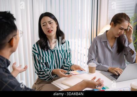 A tense business meeting where a team discusses design problems and project challenges. The man tries to explain solutions while one team member looks Stock Photo