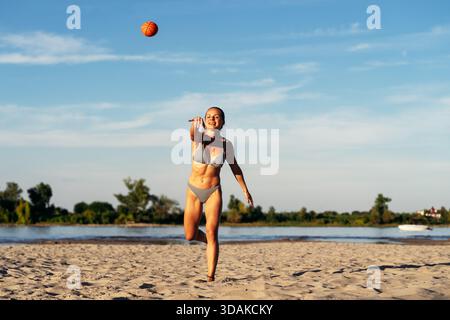 Active woman throwing a ball on the sandy beach during summer vacation Stock Photo