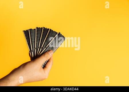 Hand holding fan of black DDR RAM sticks on yellow background, upgrade concept Stock Photo
