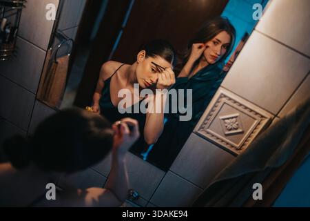 Two friends apply makeup in a bathroom mirror with moody lighting and reflections Stock Photo