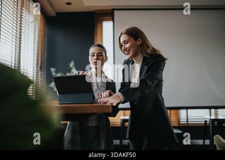 Two businesswomen collaborate at a table with a tablet in a modern office setting Stock Photo