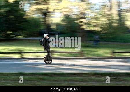 A man in a helmet is riding a motorized unicycle through a road in Central Park, New York Stock Photo
