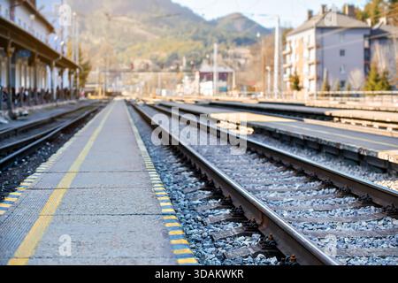 Empty train station in small city on sunny day, shallow depth of field photo, focus on concrete platform and steel rail foreground Stock Photo