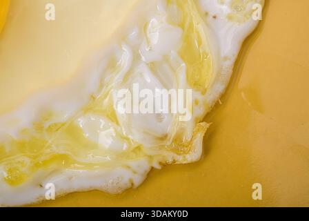 Close-up of egg white spreading across a yellow surface. Stock Photo