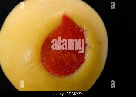 Stuffed green olive with red pimento filling in extreme close-up. Stock Photo