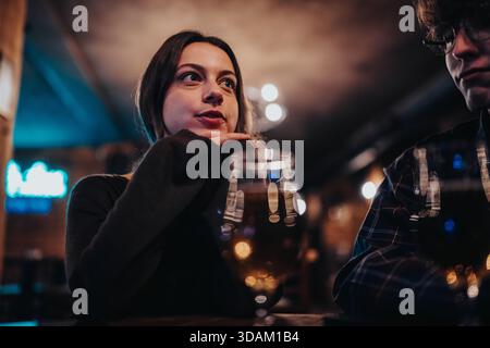 Two friends chat over drinks in a dimly lit urban bar at night and share a moment Stock Photo