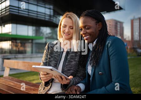 Businesswomen collaborating on tablet outdoors discussing project Stock Photo