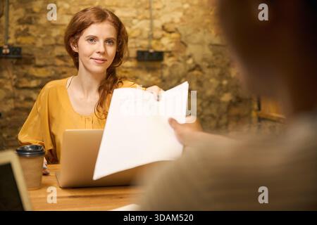 Red-haired woman reviewing documents while a man writes Stock Photo
