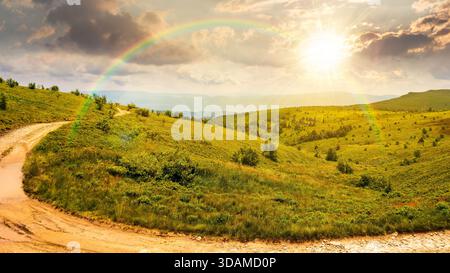 country dirt road through mountains on a summer sunset. scenic view of green rolling hills under blue sky with clouds in evening light. leadership cor Stock Photo