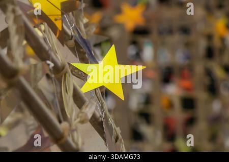 Close-up view of a bright yellow paper star tied to a decorative frame, part of a festive community display. The shallow depth of field highlights the Stock Photo