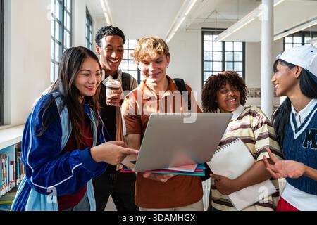 Multiethnic group of young students meeting at the library - diverse college students smiling and looking at laptop screen in library, actively engage Stock Photo