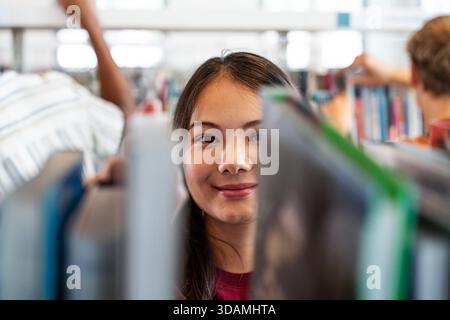 Young asian woman smiling while looking through books in a public library, representing learning, education, and knowledge acquisition for studying or Stock Photo