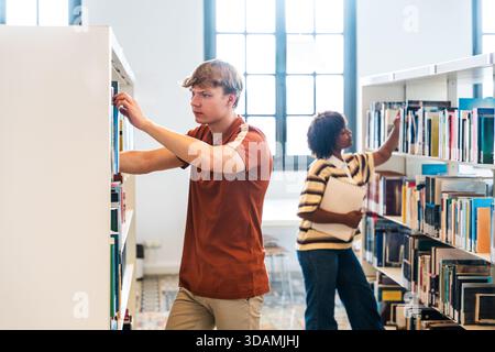 Multiethnic group of young students meeting at the library - young diverse students focused on finding books from shelves, engaged in learning and res Stock Photo