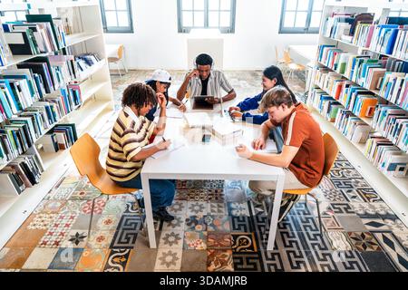 Multiethnic group of young students meeting at the library - diverse group of young students collaborating and learning at a white table in a bright m Stock Photo
