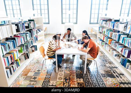 Multiethnic group of young students meeting at the library - young diverse students collaborating, learning, and doing homework at a table in a modern Stock Photo