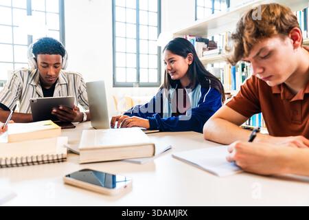 Multiethnic group of young students meeting at the library - group of diverse young students collaborating on school project, using digital tablet, la Stock Photo
