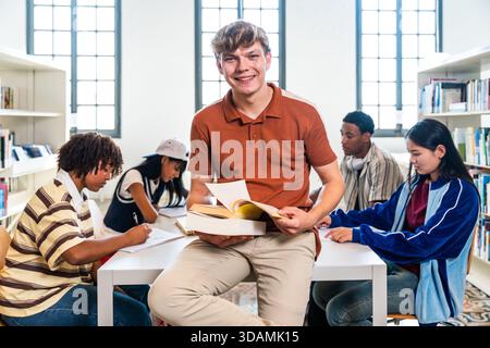 Young students actively engaging in focused learning and collaborative study, reading books and writing notes together at tables in a bright universit Stock Photo