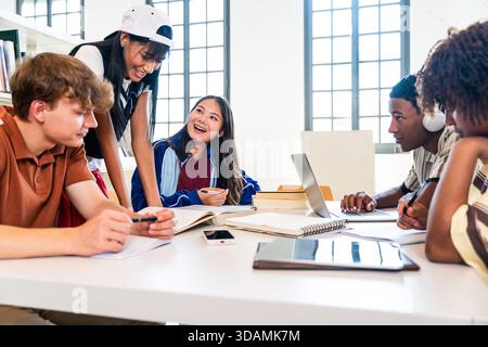 Multiethnic group of young students meeting at the library - diverse group of young students collaborating and learning at a study table in a bright l Stock Photo