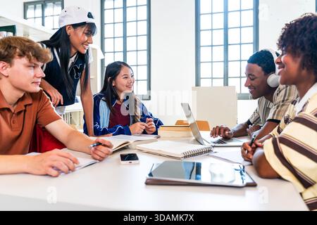 Multiethnic group of young students meeting at the library - diverse young students working together, using laptops and books, sharing ideas for acade Stock Photo